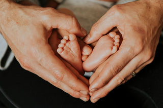 Two pairs of hands holding a baby's feet together in a heart shape.
