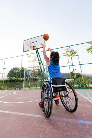 A woman in a wheelchair playing basketball at an outdoor court.