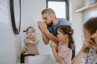 Father blowing soap bubbles in the bathroom with three daughters