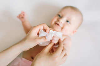 Soft focus on a baby holding a dry cotton wipe, which is in focus in the foreground