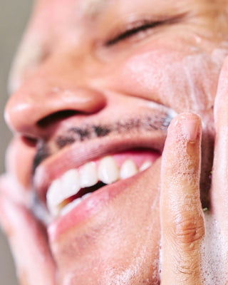 Smiling man washing his face with gentle foaming cleanser