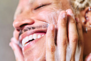 Smiling man washing his face with gentle foaming cleanser